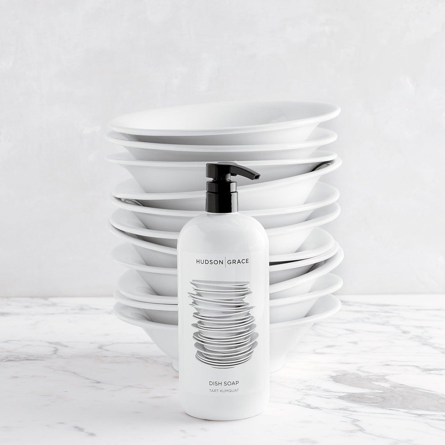 Hudson Grace Tart Kumquat Dish Soap, 32 oz, white bottle with black pump, stacked white bowls behind.