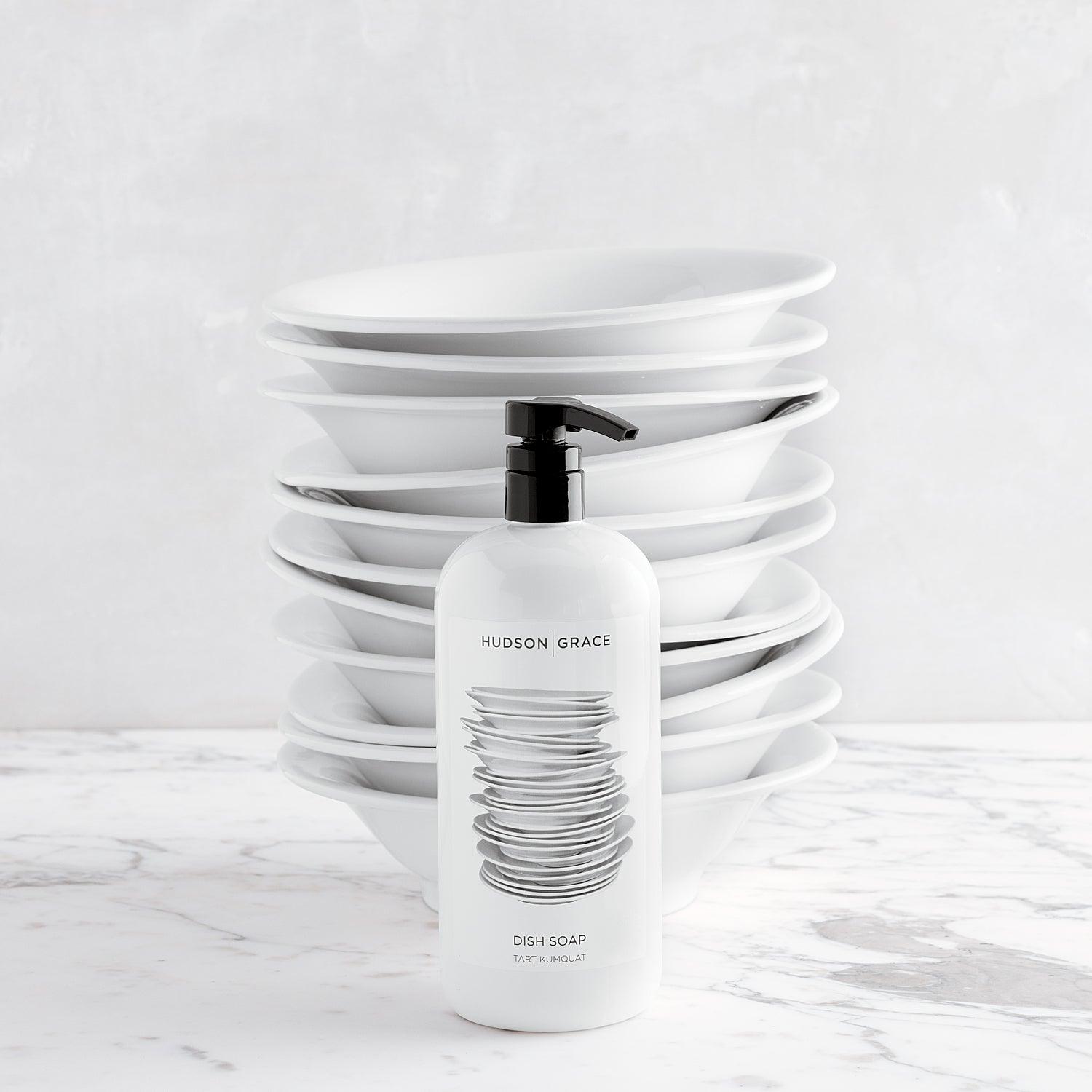 Hudson Grace Tart Kumquat Dish Soap, 32 oz, white bottle with black pump, stacked white bowls behind.