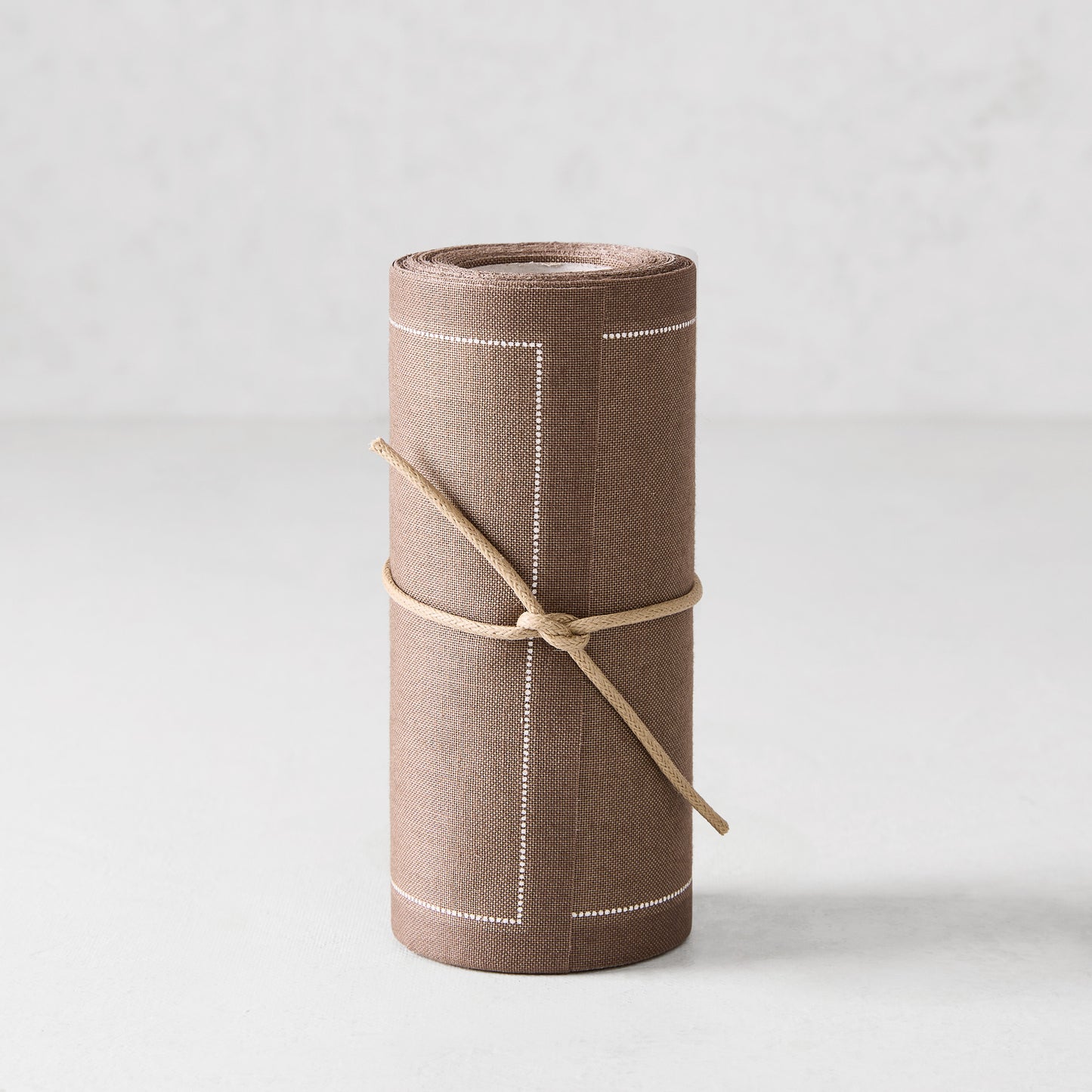Taupe brown tear-off cotton cocktail napkin roll, tied with twine, featuring white dotted borders.