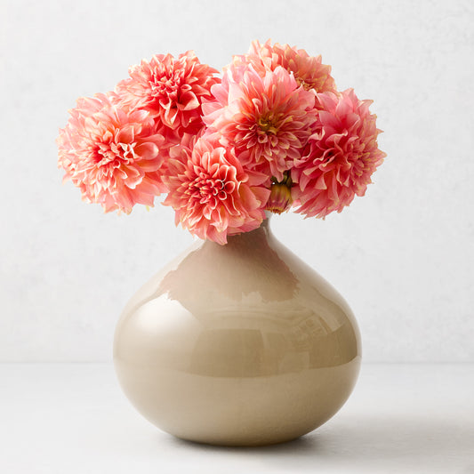Taupe hand-blown glass vase with a round, geometric silhouette filled with pink dahlia flowers.