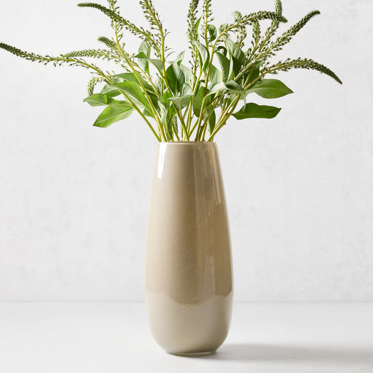 Hand-blown taupe glass vase with a sleek, geometric silhouette and curved edges, 15 inches tall, filled with green stems.