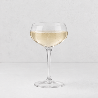 Tavola coupe glass filled with sparkling champagne on a light grey background.