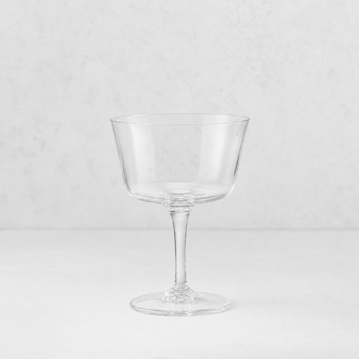 Clear glass coupe cocktail glass with a wide bowl and slender stem on a white background.