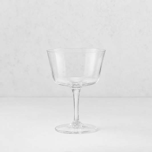 Clear glass coupe cocktail glass with a wide bowl and slender stem on a white background.