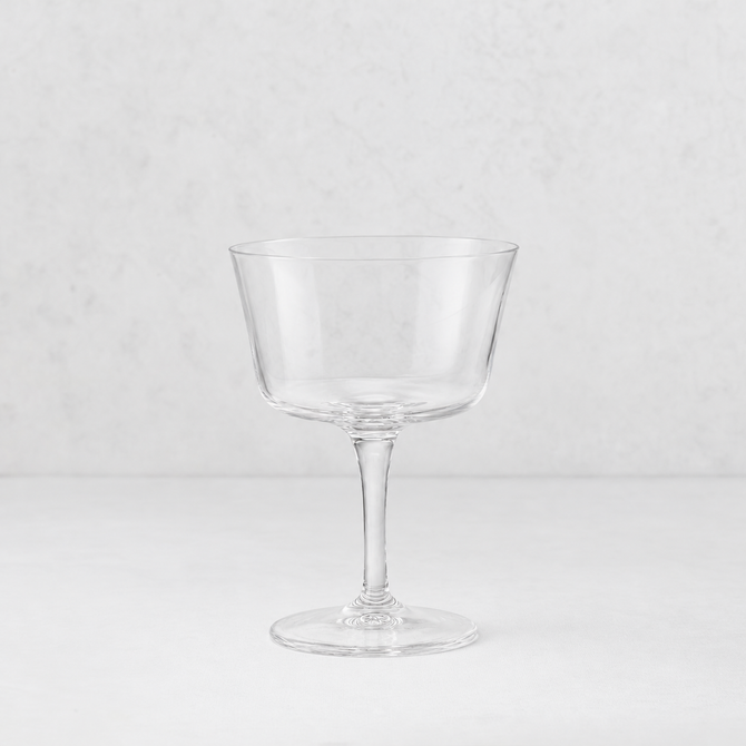 Clear glass coupe cocktail glass with a wide bowl and slender stem on a white background.