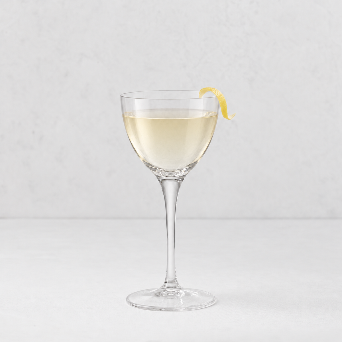 Tavola Nic and Nora 5.25oz clear glass coupe with a seamless stem and a thin rim, garnished with a lemon twist.