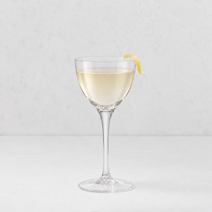 Tavola Nic and Nora 5.25oz clear glass coupe with a seamless stem and a thin rim, garnished with a lemon twist.