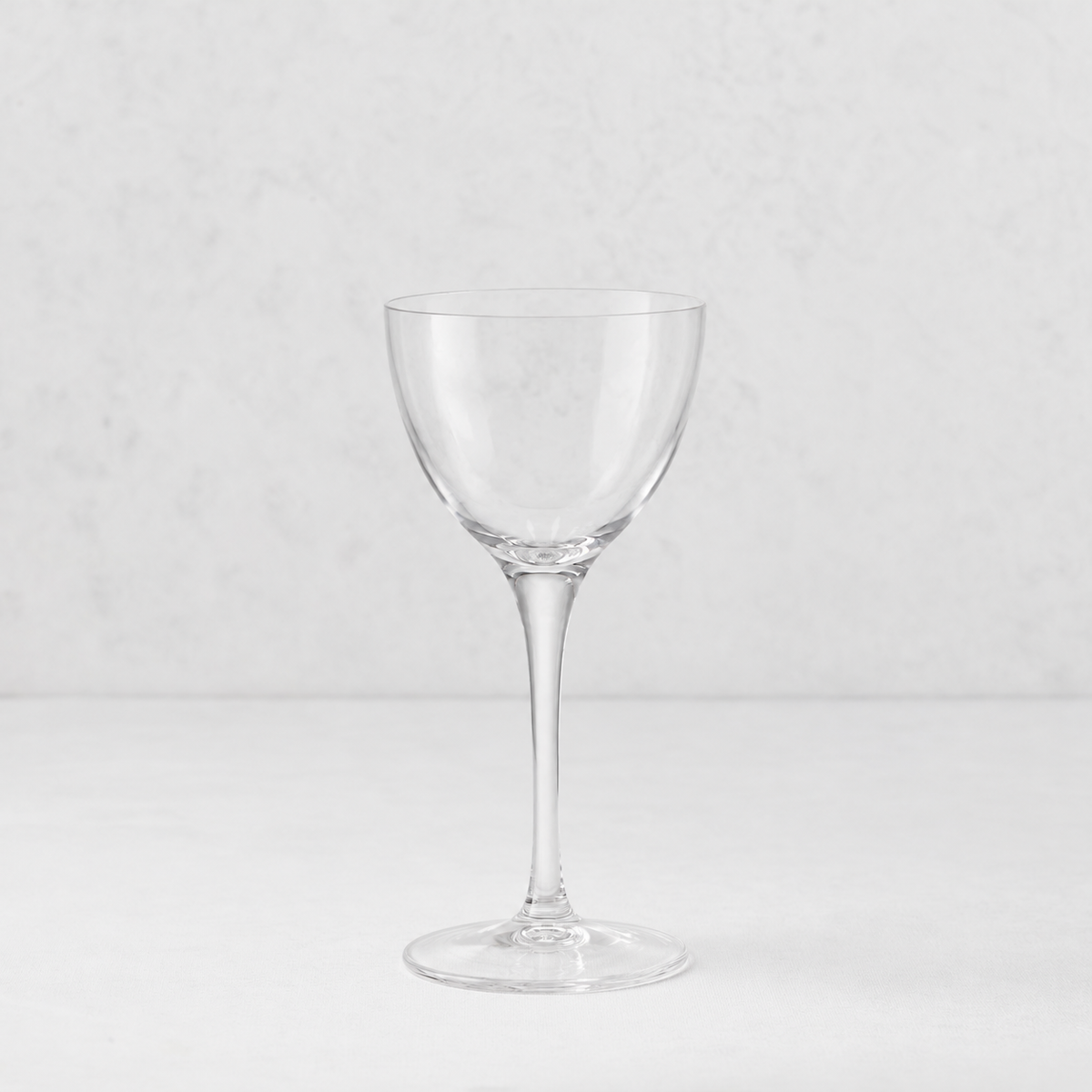 Clear glass Tavola Nic and Nora coup cocktail glass with a seamless stem and thin rim on a white surface.
