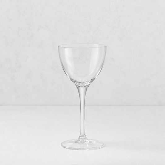 Clear glass Tavola Nic and Nora coup cocktail glass with a seamless stem and thin rim on a white surface.