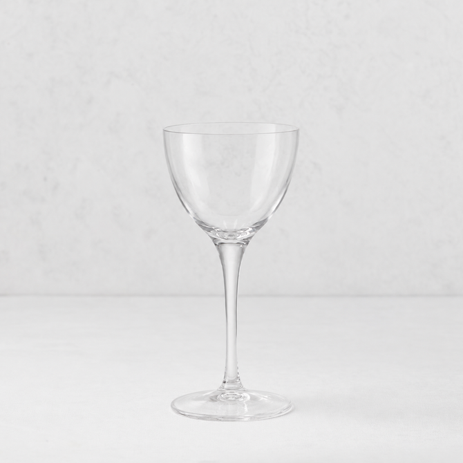 Clear glass Tavola Nic and Nora coup cocktail glass with a seamless stem and thin rim on a white surface.