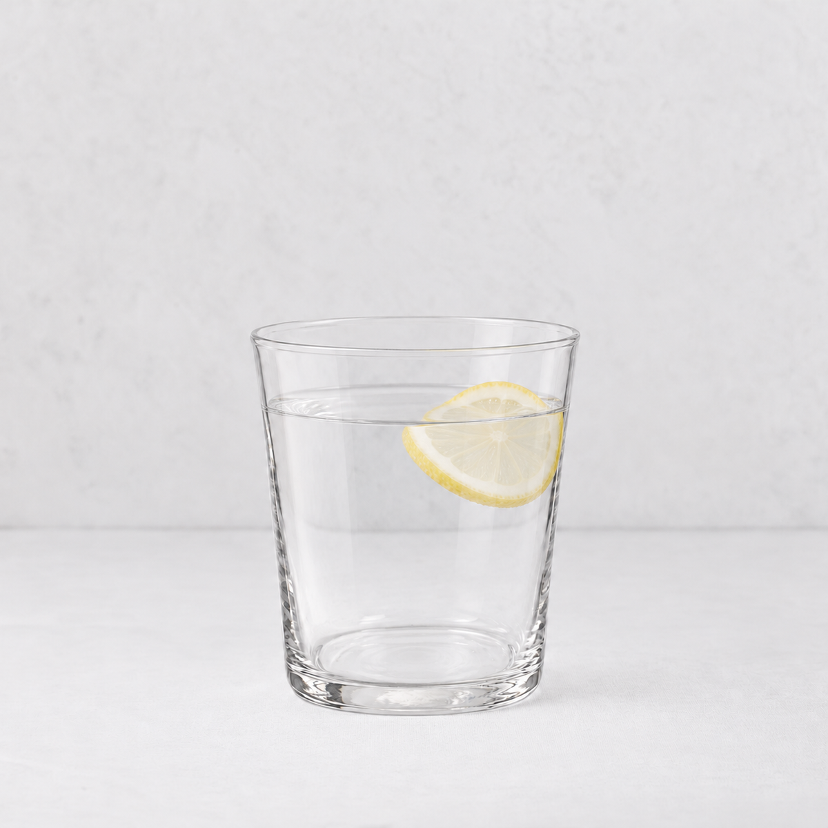 Medium Tavola tumbler made of clear glass, filled with water and a single lemon slice, on a white surface.