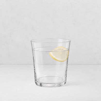 Medium Tavola tumbler made of clear glass, filled with water and a single lemon slice, on a white surface.