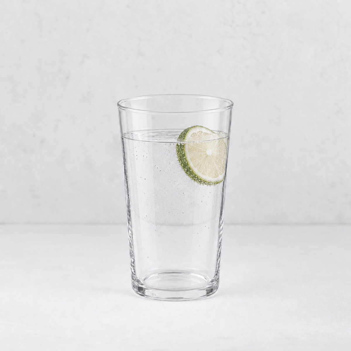 Tall clear glass Tavola tumbler filled with sparkling water and a fresh lime slice on a white background.