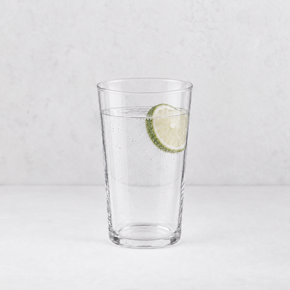 Tall clear glass Tavola tumbler filled with sparkling water and a fresh lime slice on a white background.
