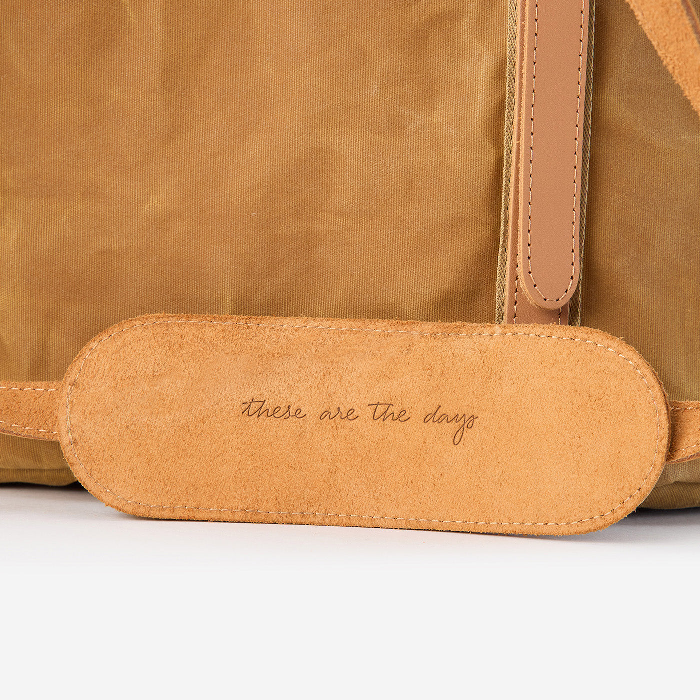 Close-up of a Goldie Picnic Bag in tan waxed canvas with a leather shoulder strap pad embossed "these are the days.