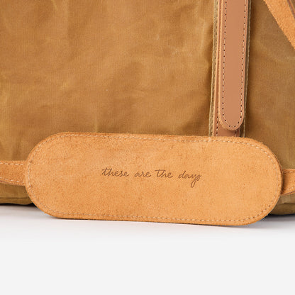 Close-up of a Goldie Picnic Bag in tan waxed canvas with a leather shoulder strap pad embossed "these are the days.