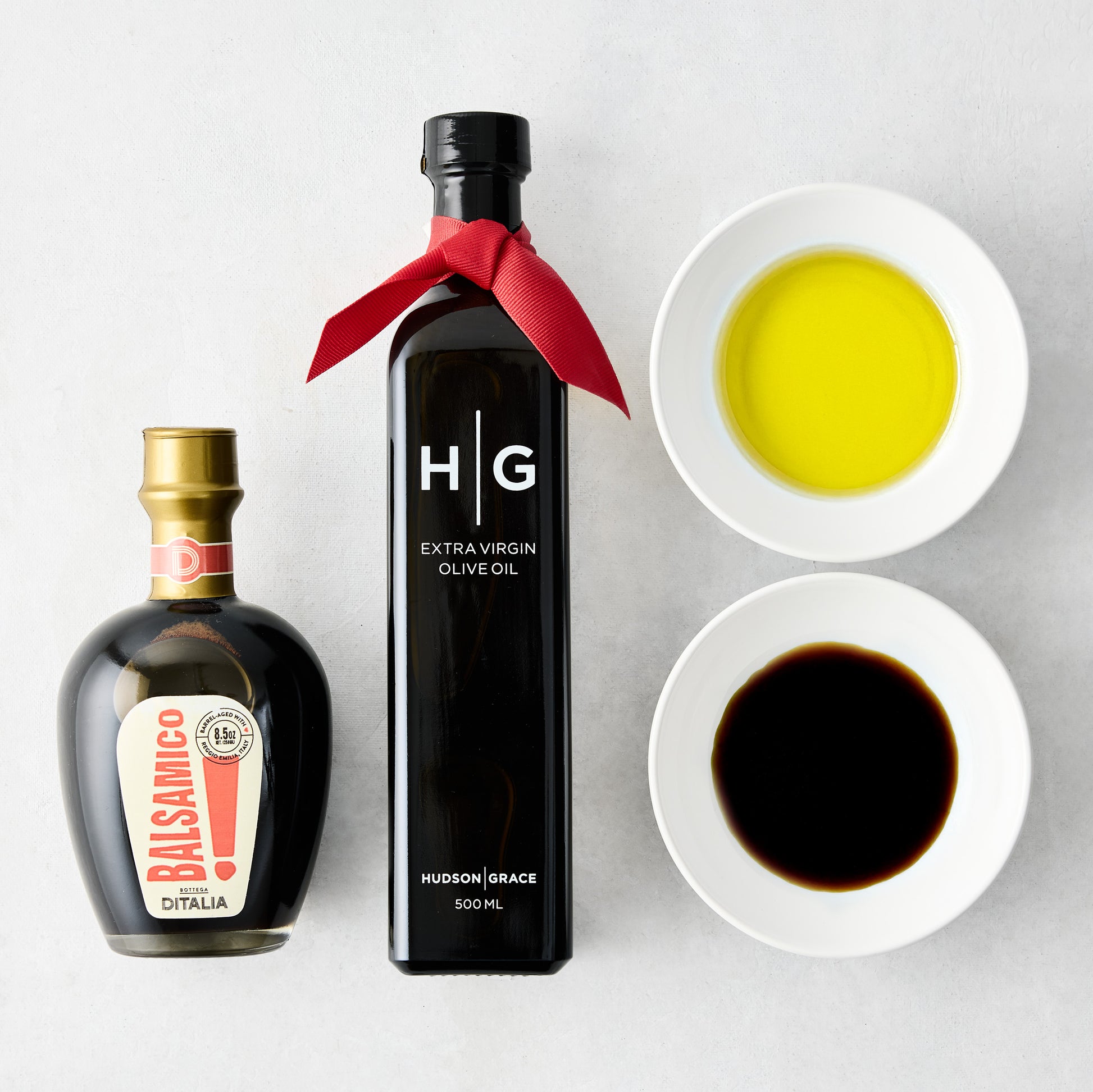 Hudson Grace olive oil, balsamic vinegar, and two white dipping bowls with oil and vinegar.