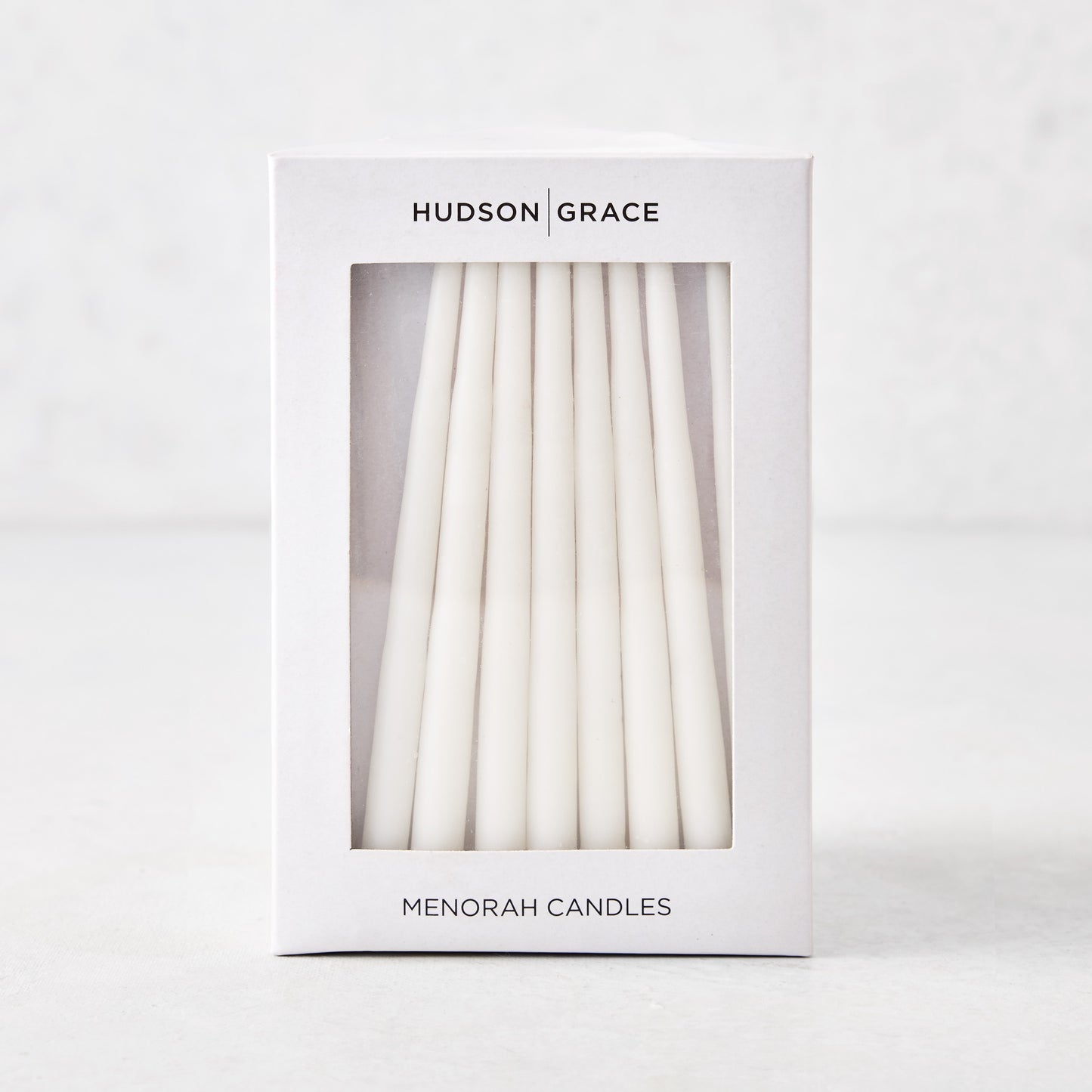 Box of 45 slender, hand-dipped white paraffin Hanukkah taper candles in white Hudson Grace packaging.