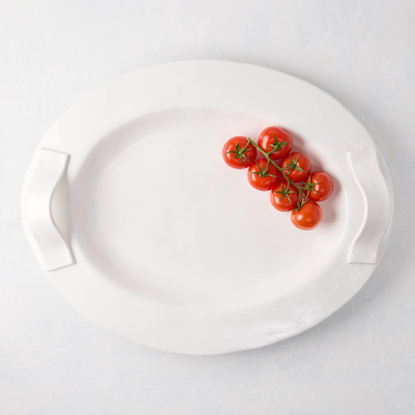 Tivoli white ceramic oval serving platter with two handles and a cluster of cherry tomatoes.