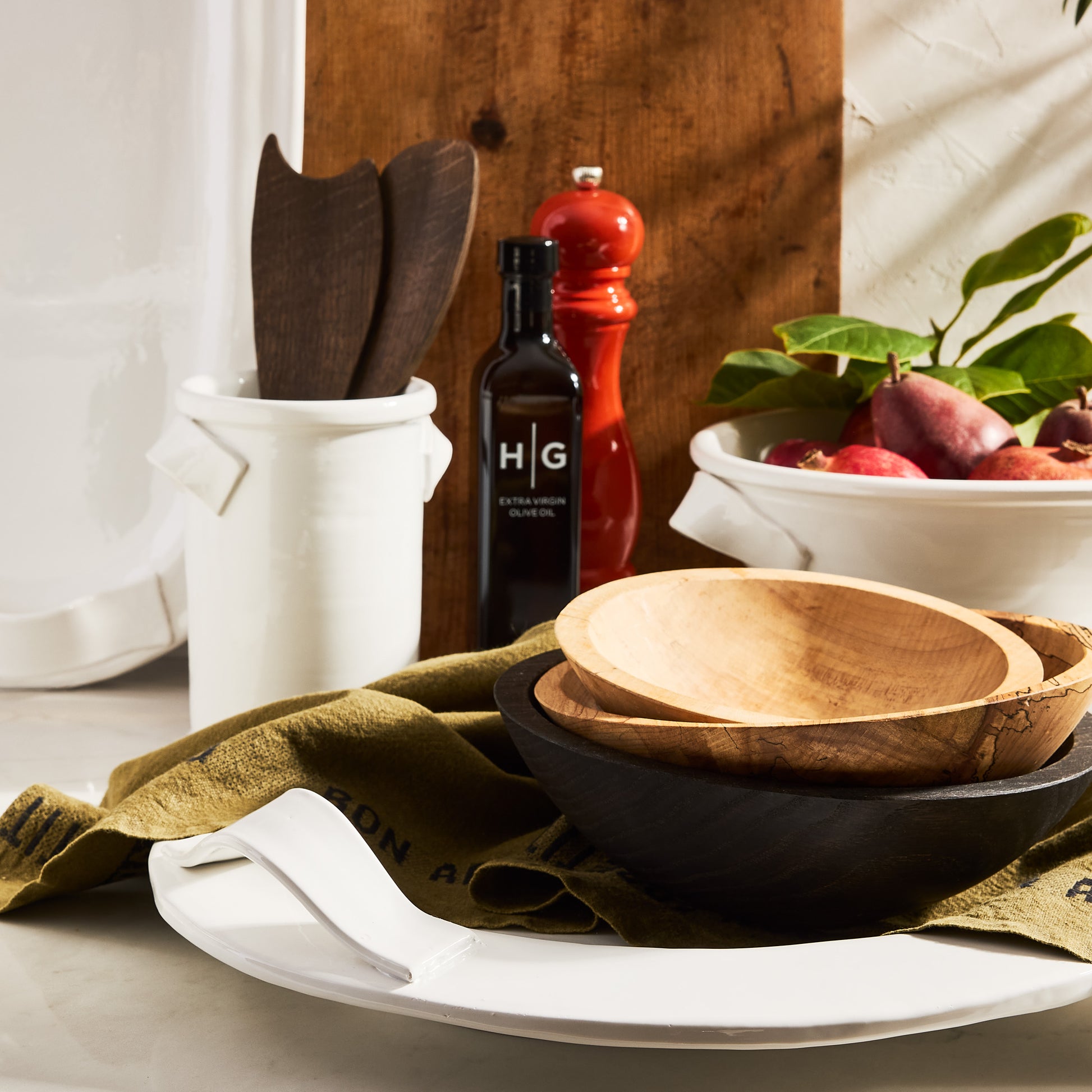 White ceramic Tivoli pedestal serve bowl with two handles, on a marble surface with wooden bowls and olive oil.