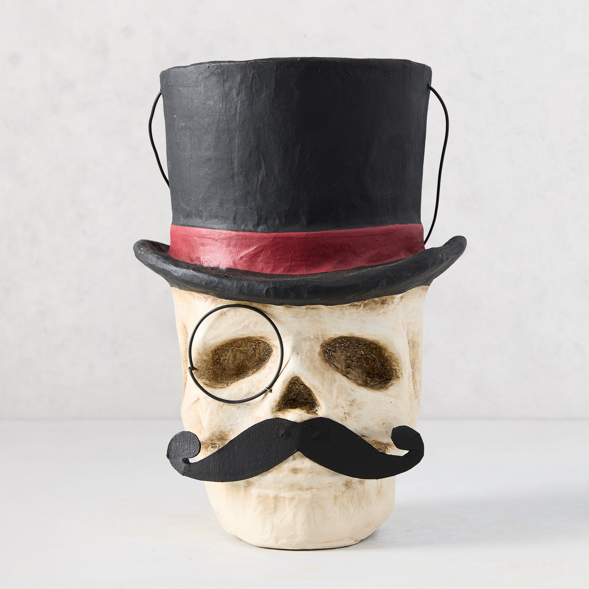 11-inch papier-mâché skull candy bucket wearing a black top hat with red band, a monocle, and a black mustache.