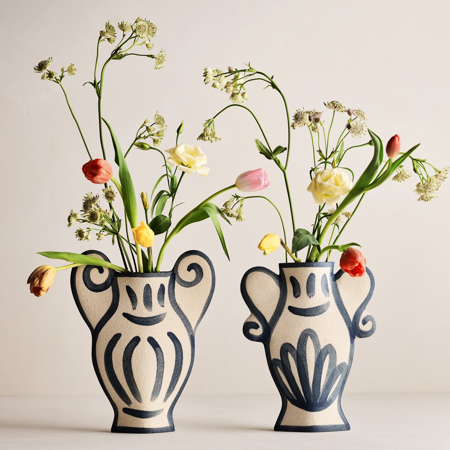 Two Trompe-L'oeil Greek Coupe Krater stoneware vases with blue detailing and colorful flowers.