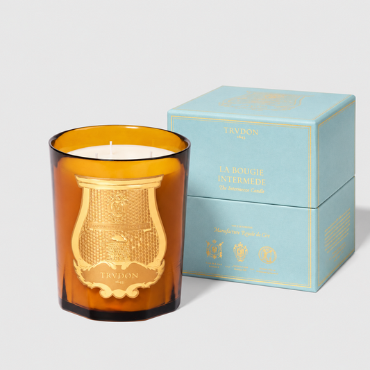 Trudon Altair Intermezzo candle in an amber glass vessel with a gold emblem, next to a light blue presentation box.