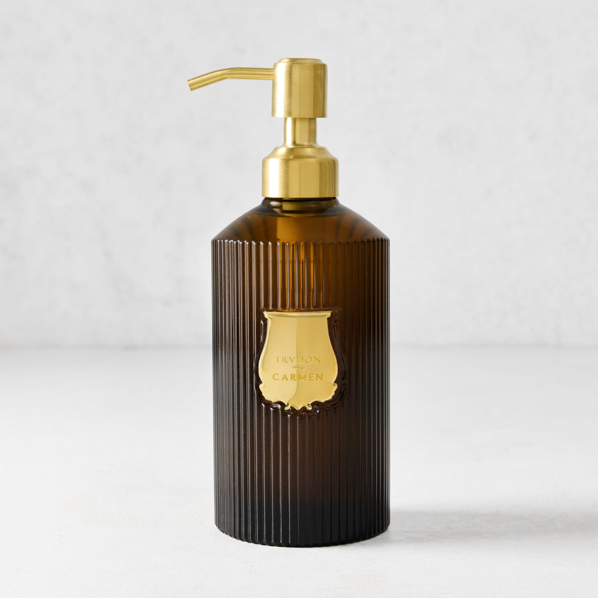 Trudon Carmen liquid hand soap in a ribbed amber glass bottle with a gold pump and label.