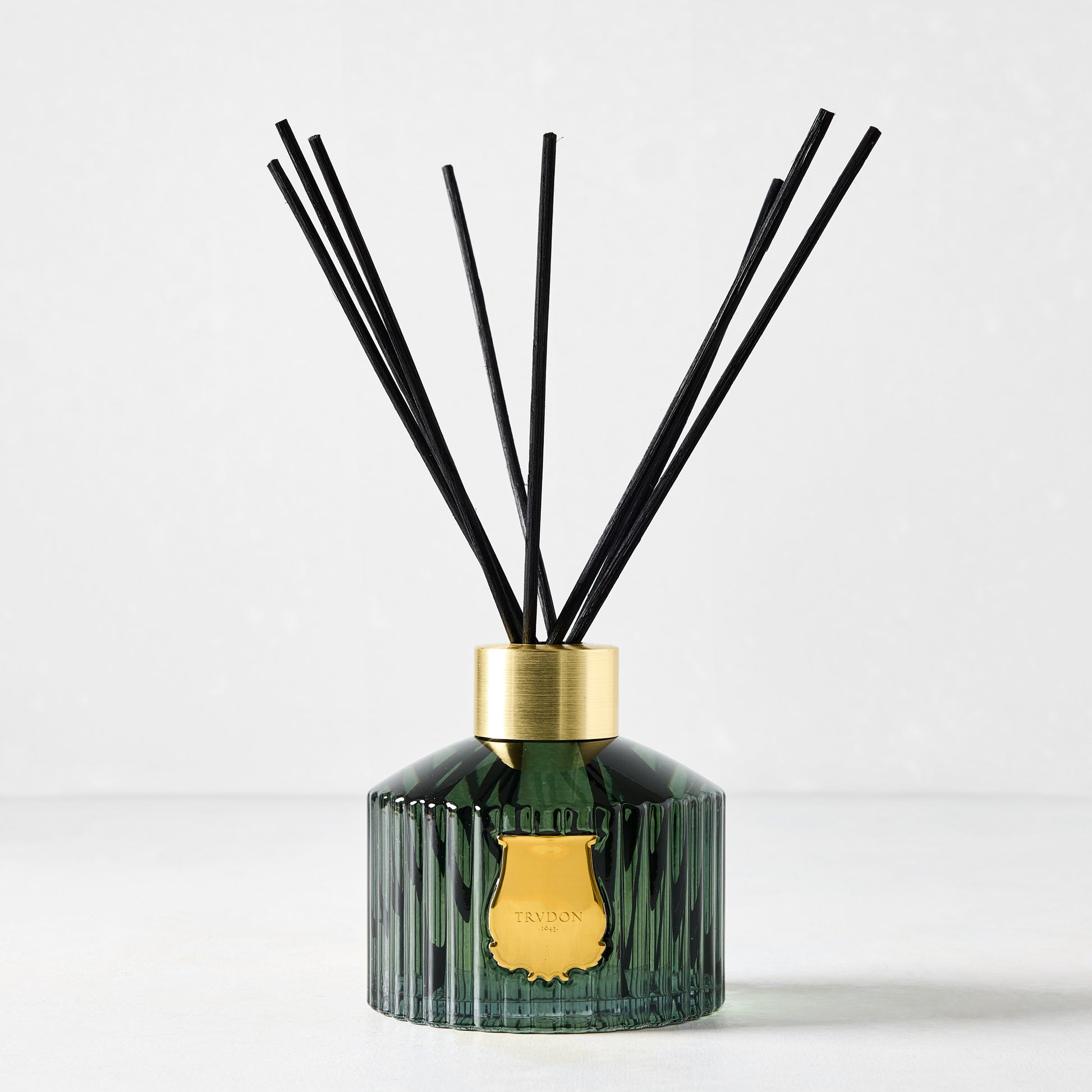 Trudon Figuerie Scented Reed Diffuser: dark green fluted glass, gold seal, black rattan sticks.