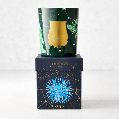 Trudon Holiday Edition Fir Classic Scented Candle in a dark green glass vessel with gold label, on a matching navy blue box with celestial design.