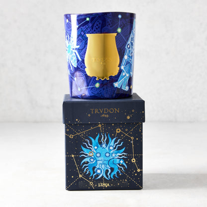 Trudon Luna Holiday Edition scented candle in a blue glass vessel with gold celestial illustrations, atop a matching box.