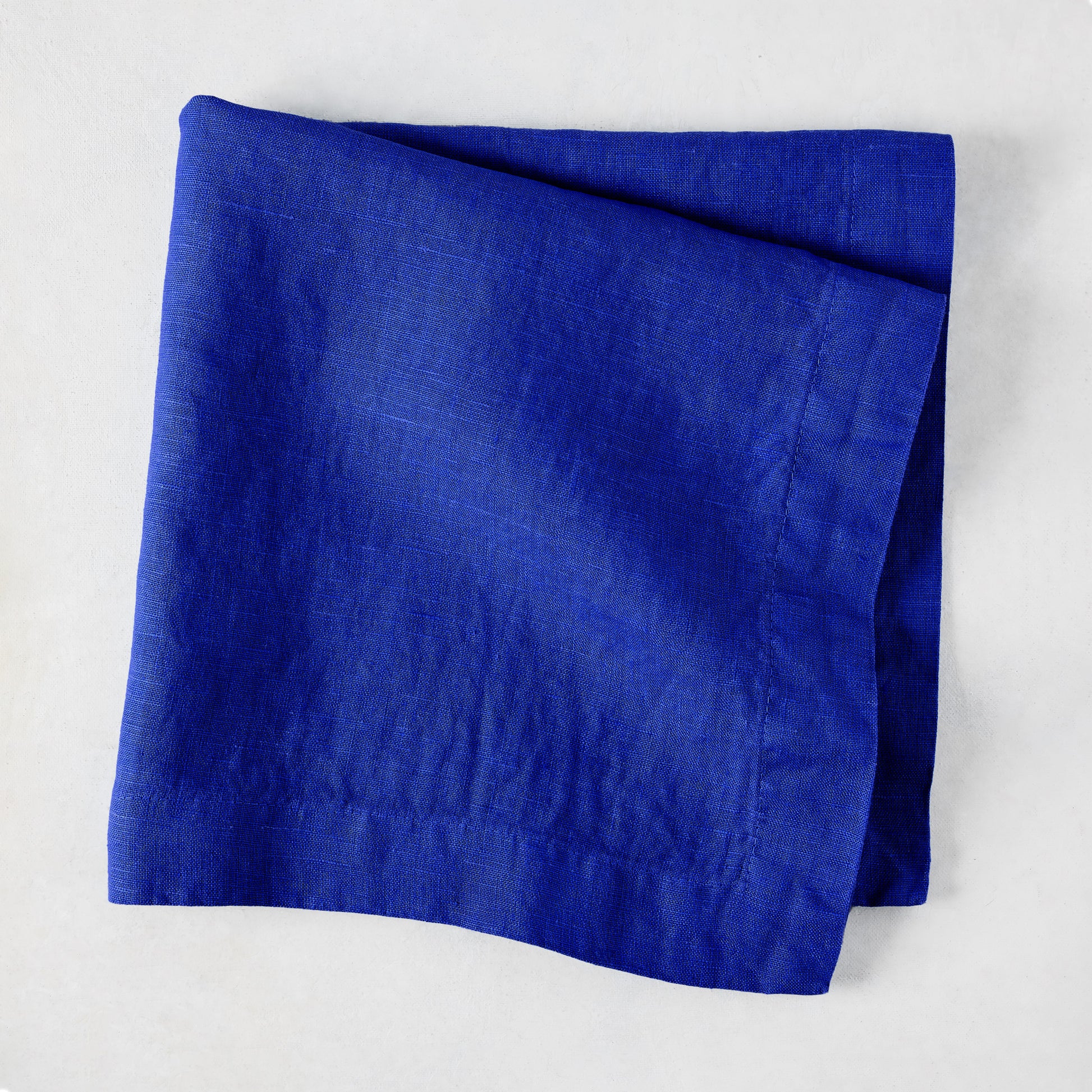 Ultramarine HG Signature hand-dyed 22" square linen napkin, folded, on a white background.