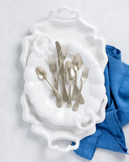Vintage Champagne 5-piece flatware set: silvery-champagne stainless steel forks, knives, and spoons on white baroque plates.