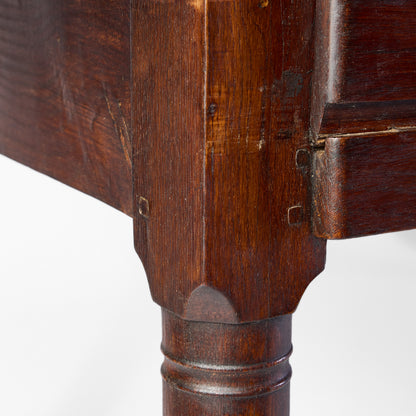 Close-up of a vintage mahogany kitchen table featuring dark wood grain, joinery details, and a slender turned leg.