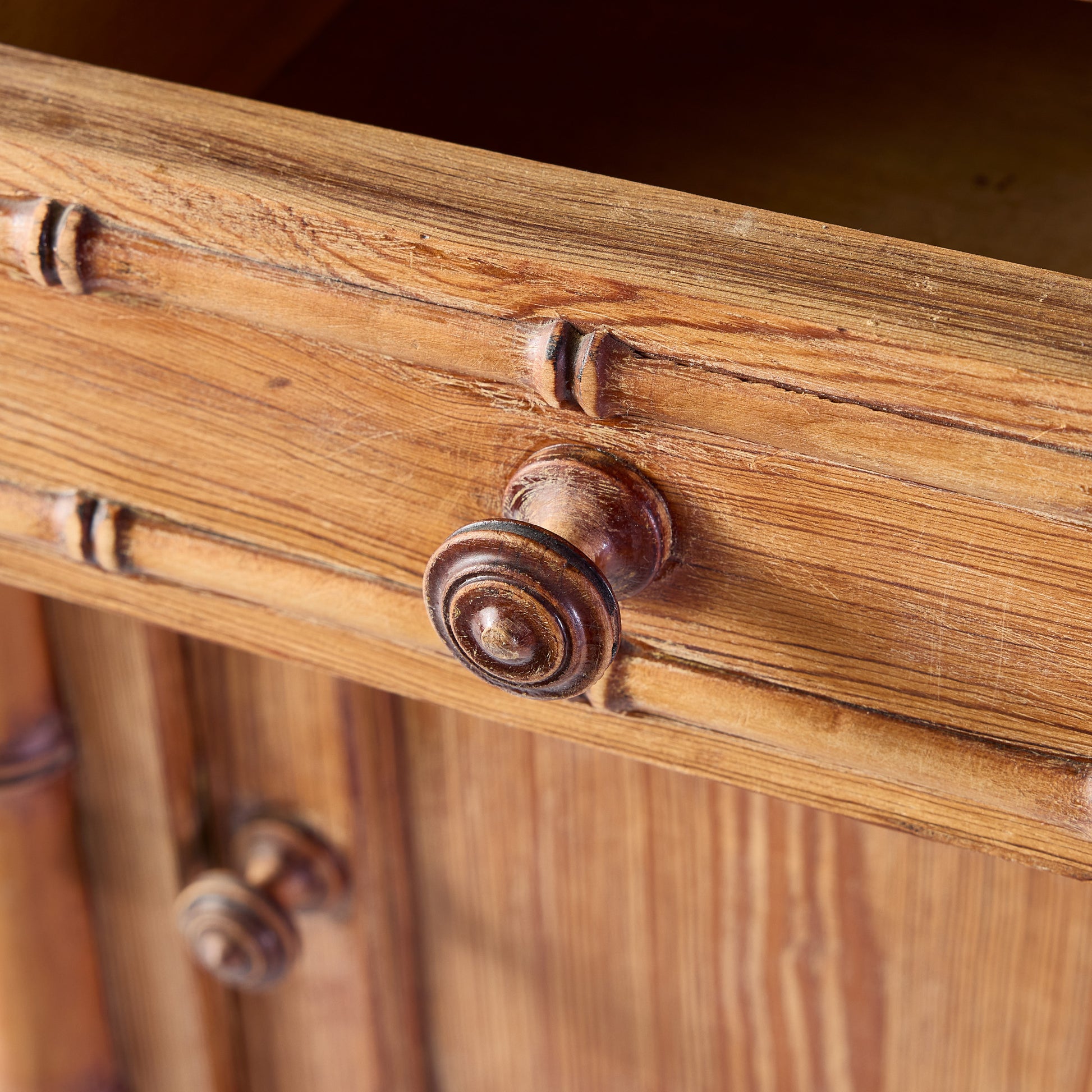 Close-up of a vintage oak wood nightstand drawer with bamboo-style carving and a round wooden knob.