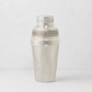 Vintage silverplate cocktail shaker with a textured finish and polished bands against a light gray background.