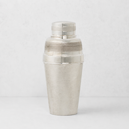 Vintage silverplate cocktail shaker with a textured finish and polished bands against a light gray background.