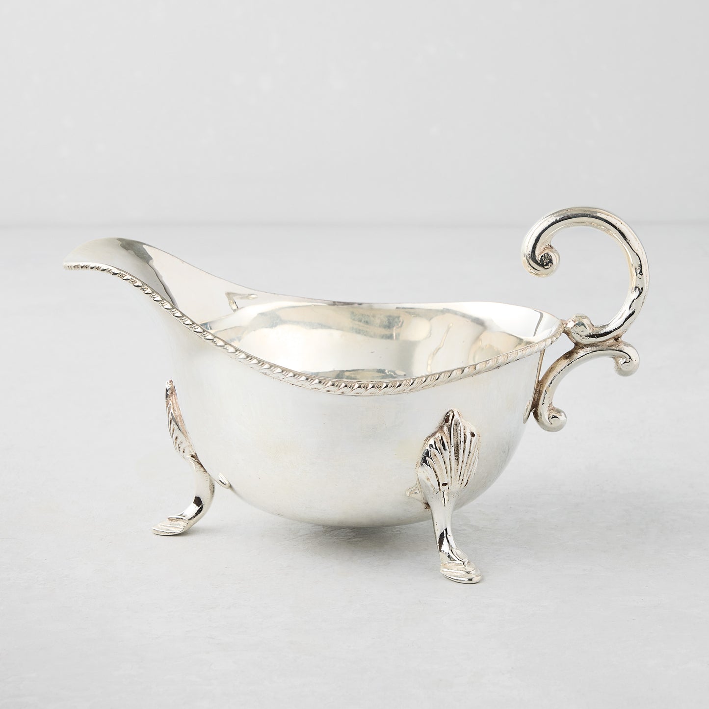 Vintage silverplate Driscoll gravy boat with ornate handle and feet.