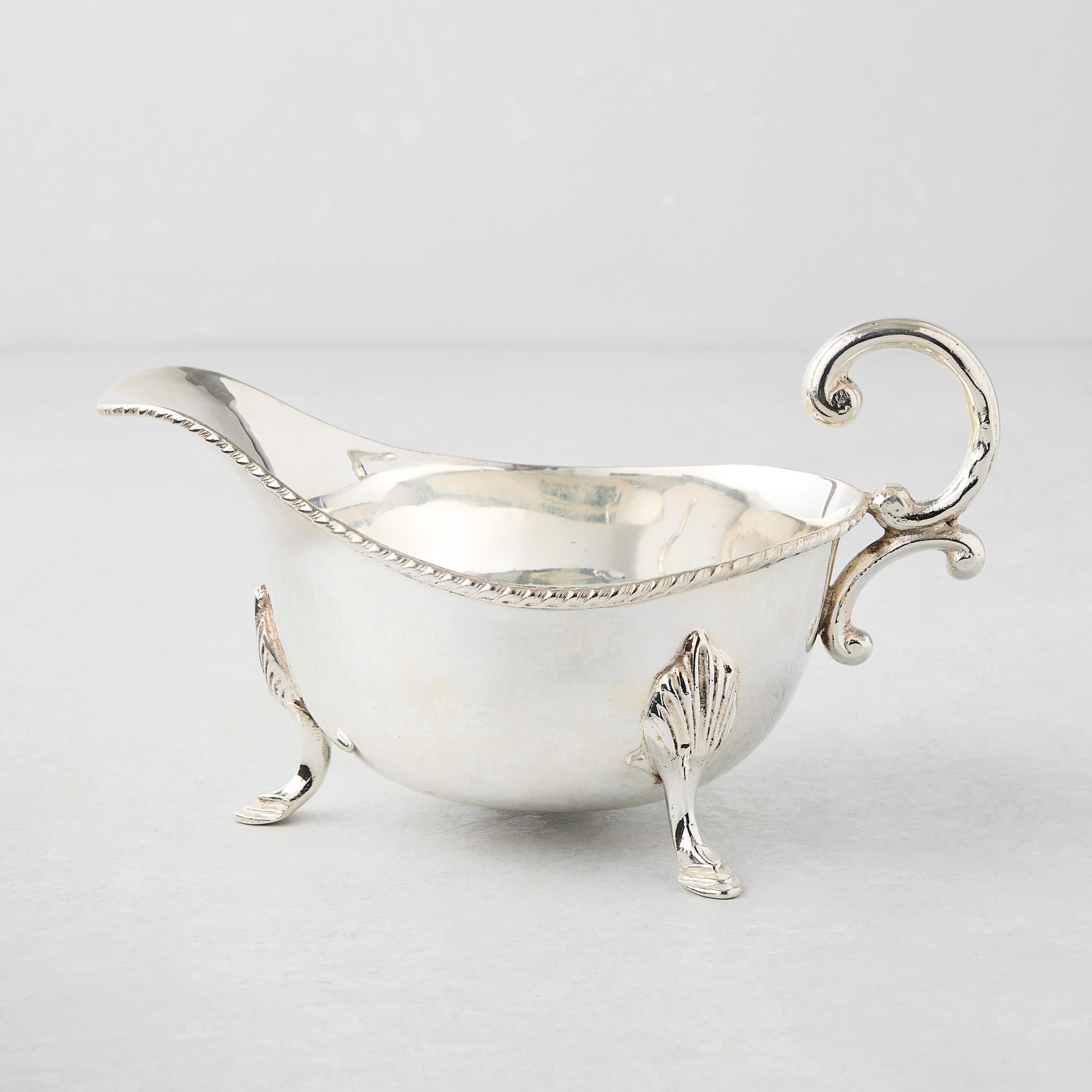 Vintage silverplate Driscoll gravy boat with ornate handle and feet.