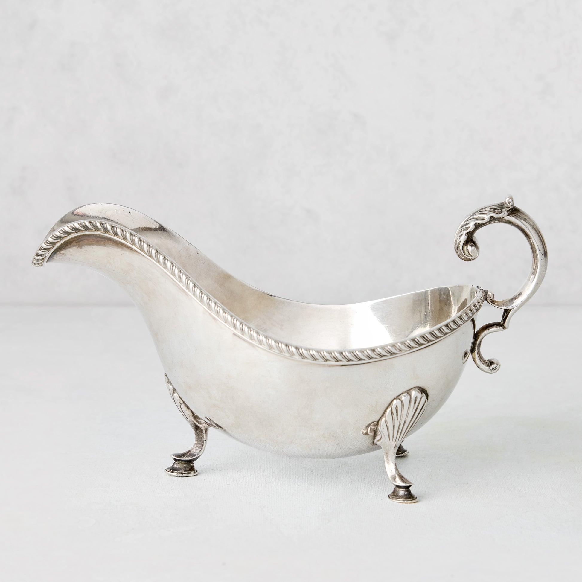 Vintage silverplate gravy boat with ornate handle, rope trim, and shell feet.