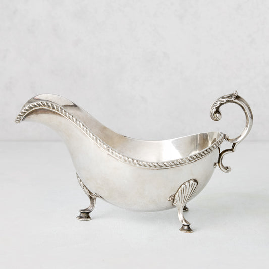 Vintage silverplate gravy boat with ornate handle, rope trim, and shell feet.