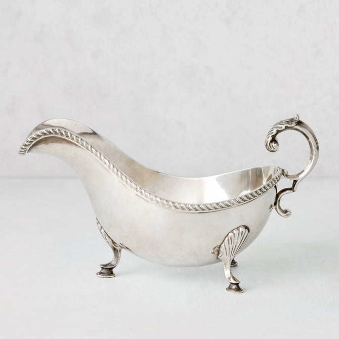 Vintage silverplate gravy boat with ornate handle, rope trim, and shell feet.