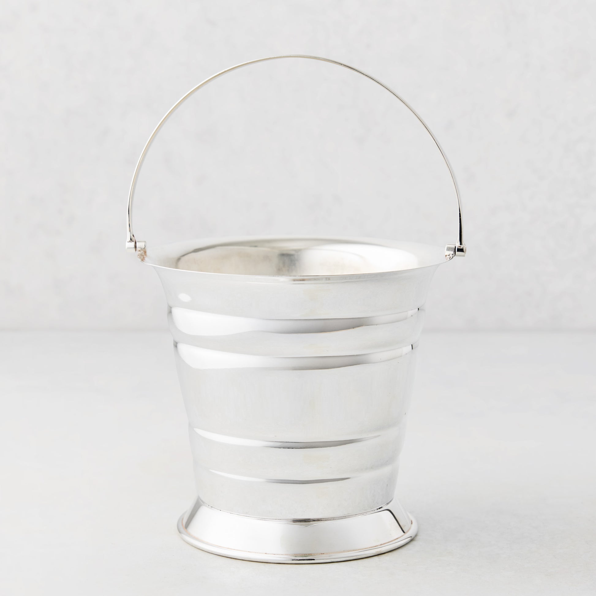 Vintage silverplate ice bucket with a polished finish, flared base, and a thin arched handle.