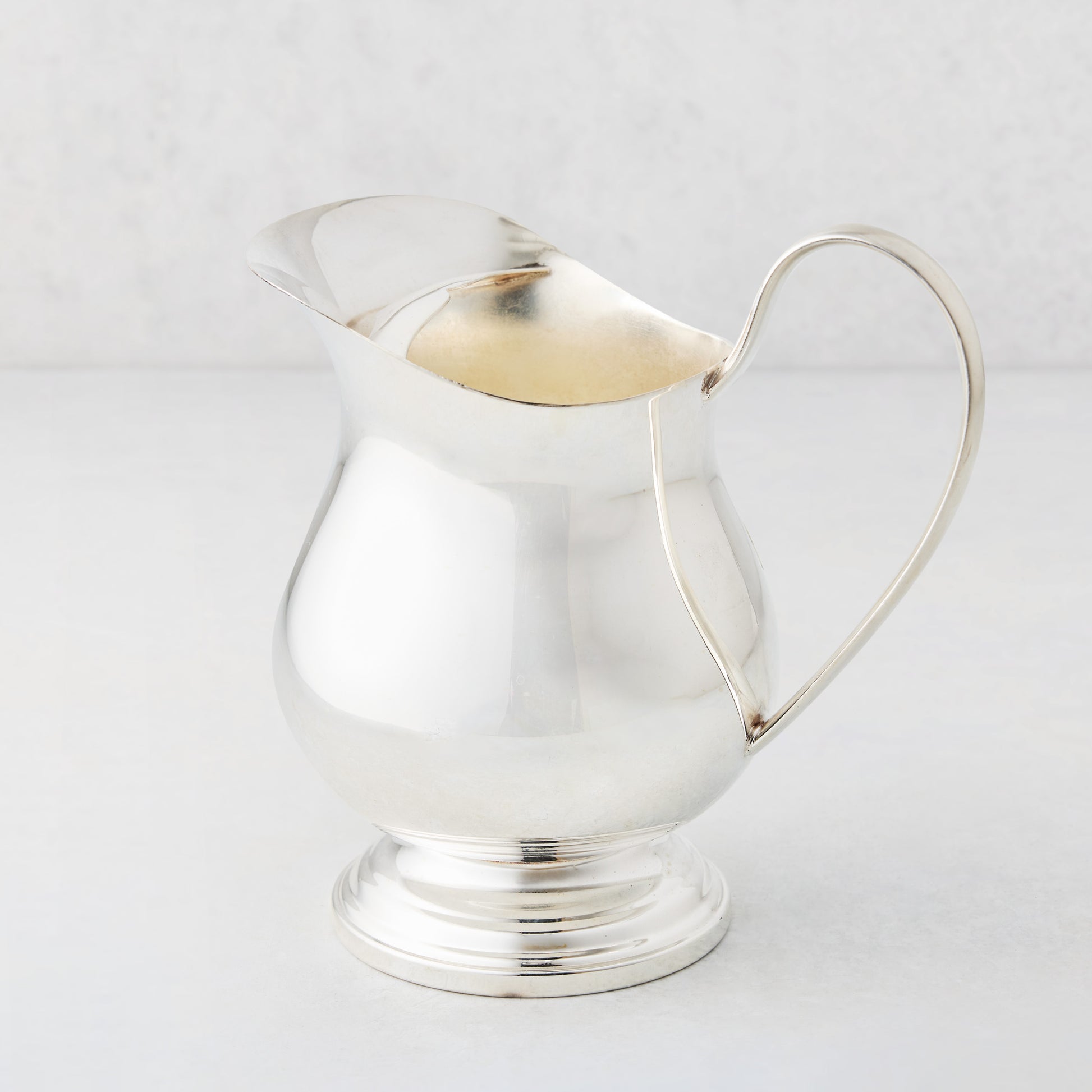 8-inch vintage silverplate Pauline jug with a polished finish, curved handle, and pedestal base.