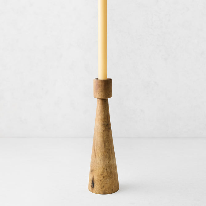 Hand-carved walnut wood candlestick with a geometric tapered base and a cream taper candle on a white background.