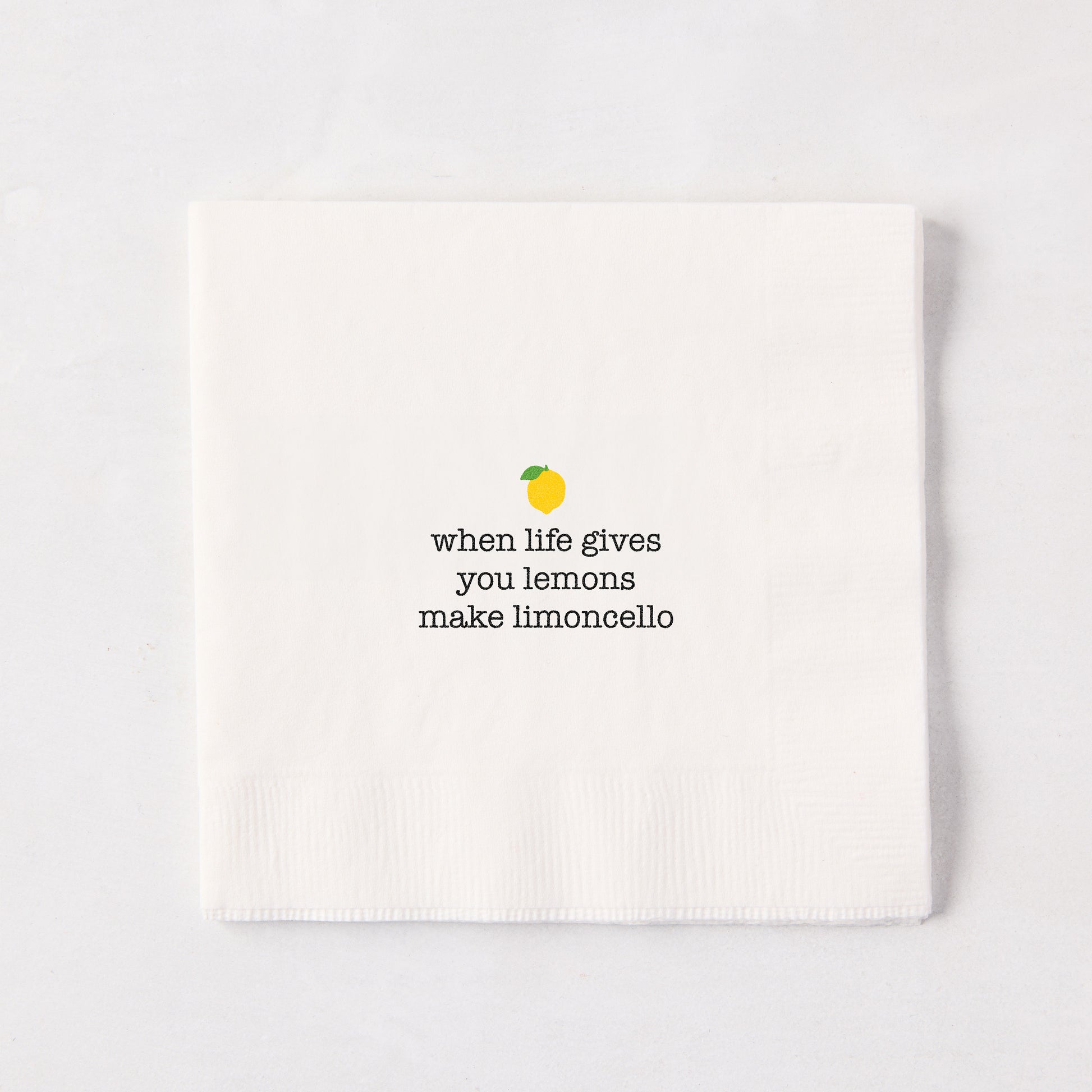 White 5.5" square paper cocktail napkin with "when life gives you lemons make limoncello" text and lemon graphic.