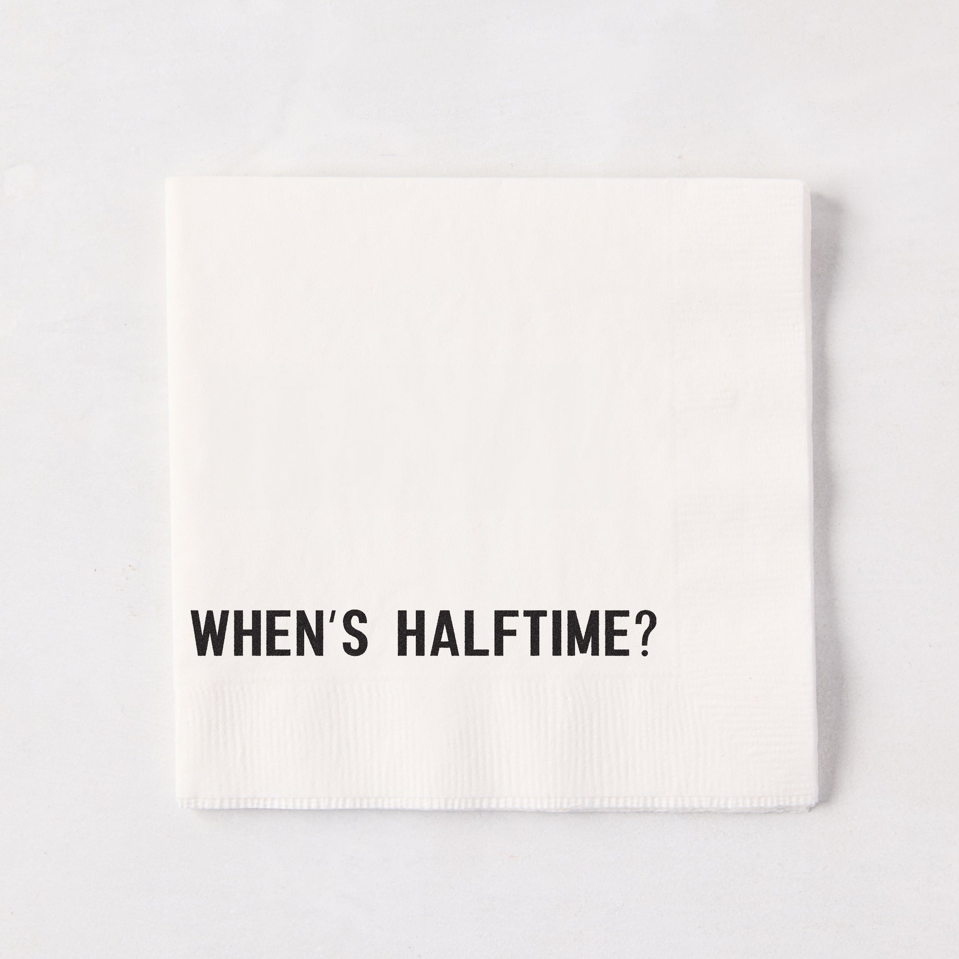 White 5.5" square paper cocktail napkin with "WHEN'S HALFTIME?" in black text.