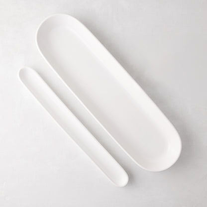 Two white ceramic oval baguette serving trays, one long and one shorter, on a light background.