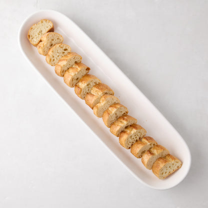 White ceramic narrow oval baguette serving tray with sliced bread.