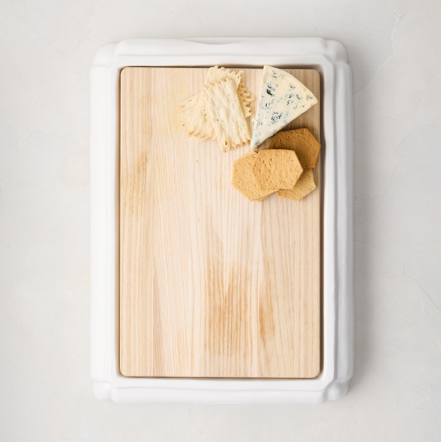 White ceramic handled cutting board with oak wood, blue cheese, and crackers.